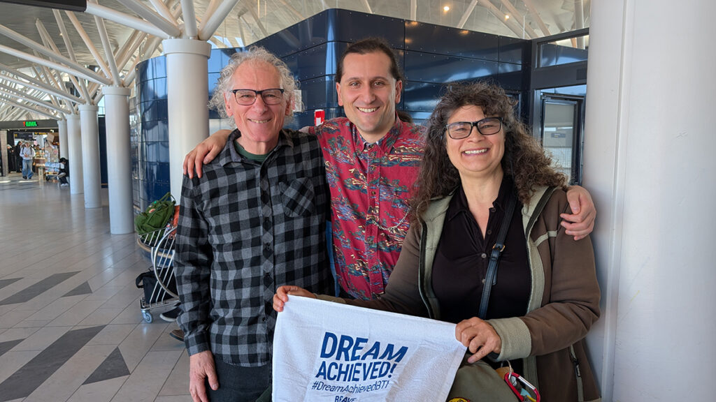 Three people posing smiling holding a sign Dream Achieved.