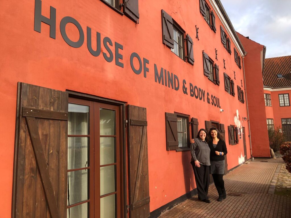 Two women posing in front of a red building with wooden shutters