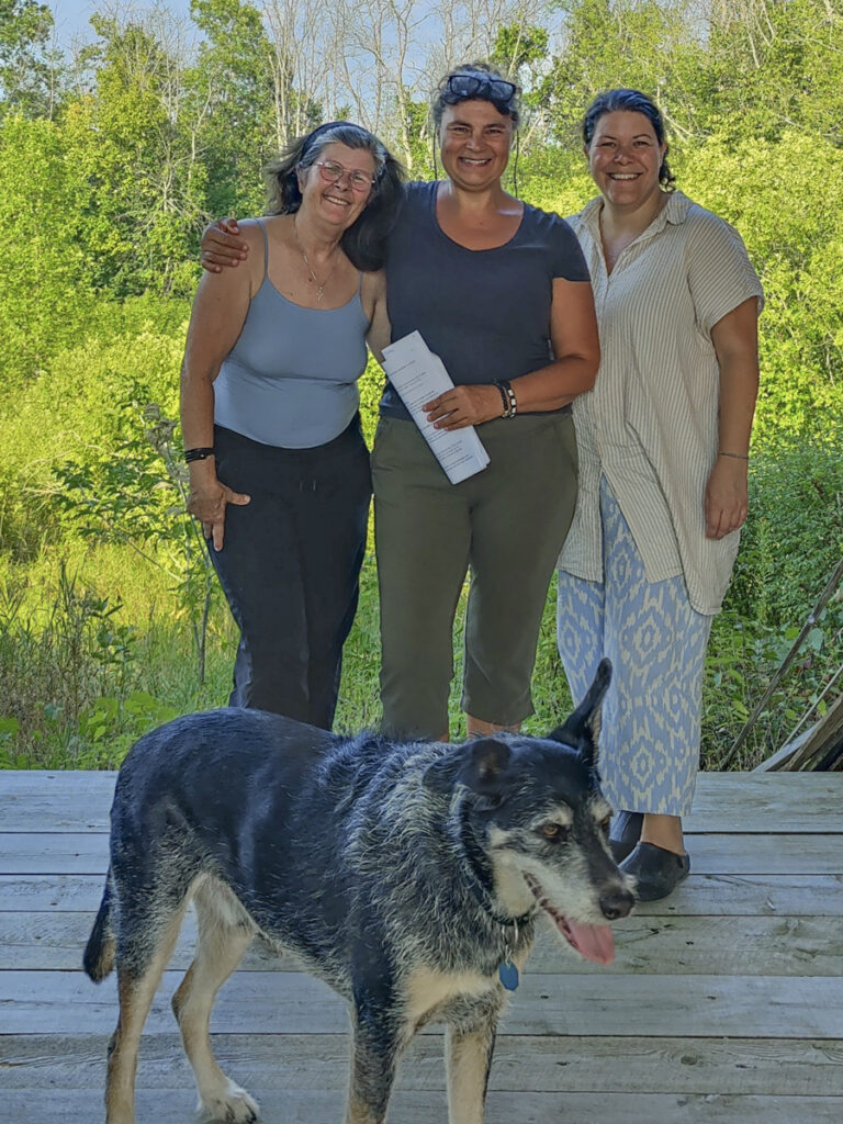 three women standing for photo with dog